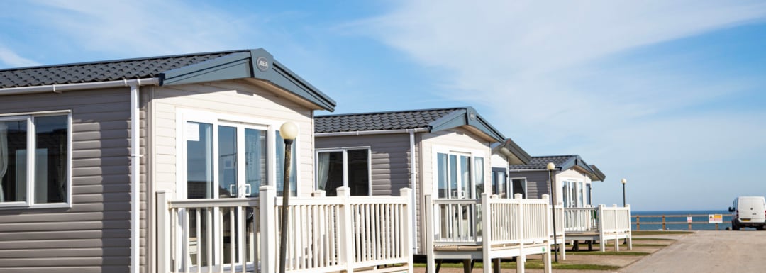 Wide angle shot of three holiday homes featuring balconies, situated alongside the sea.