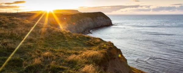 Wide angle shot of the Skirlington coastline, taken from the cliffs looking over the water with a bright lense flare.
